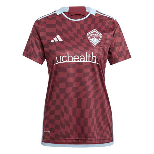 Front view of a burgundy soccer jersey featuring a warped geometric checkered pattern, white Adidas stripes on the shoulders, the team crest, and the UCHealth sponsor logo across the chest.
