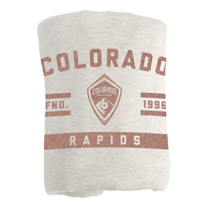 A folded light oatmeal colored blanket featuring a distressed brown Colorado Rapids graphic print, shown against a plain white background.
