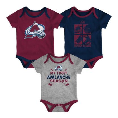 Three Colorado Avalanche baby bodysuits arranged together on a white background: a burgundy short-sleeve bodysuit with the Avalanche logo, a navy short-sleeve bodysuit with a hockey legend graphic, and a heather gray short-sleeve bodysuit with 'My First Avalanche Season' text and graphics.