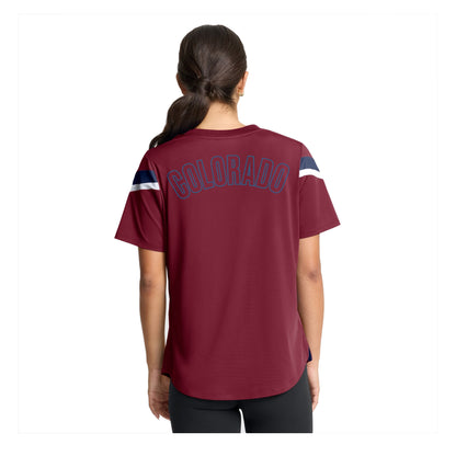 A woman viewed from the back wearing a burgundy T-shirt with 'COLORADO' arched across the upper back in navy outlined lettering, plus navy and white sleeve stripes, against a plain white background.