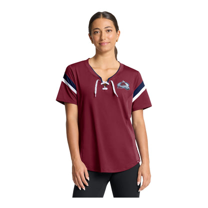 A woman modeling a short-sleeve burgundy t-shirt with a lace-up, white drawstrings, navy and white sleeve stripes, and a Colorado Avalanche logo on the left chest, set against a plain white background.