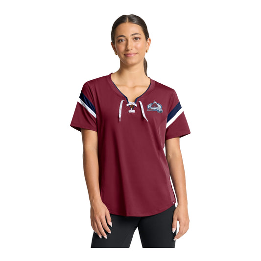 A woman modeling a short-sleeve burgundy t-shirt with a lace-up, white drawstrings, navy and white sleeve stripes, and a Colorado Avalanche logo on the left chest, set against a plain white background.